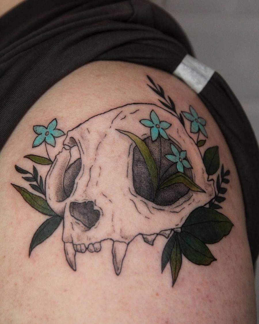 Tatuaje a color de una calavera con flores turquesa en el hombro