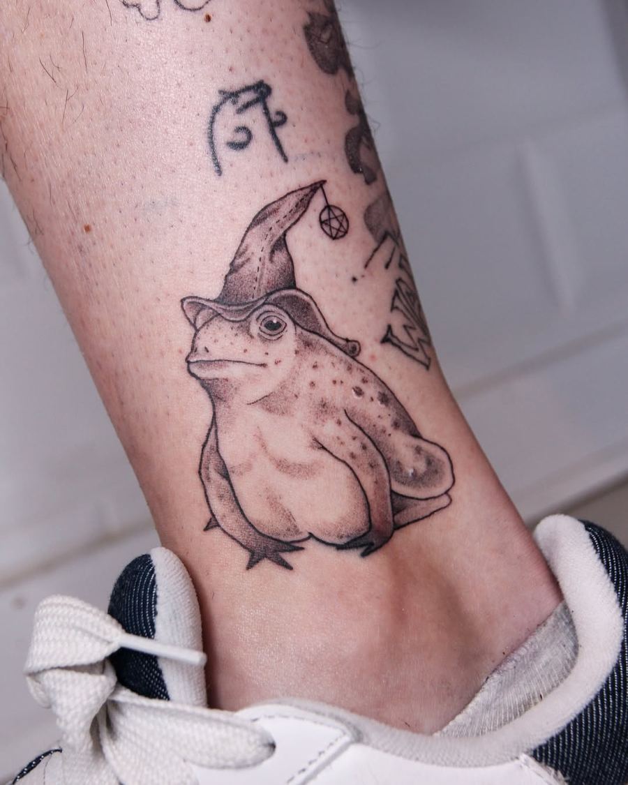 Tatuaje ilustrativo de una rana con sombrero de mago en el tobillo